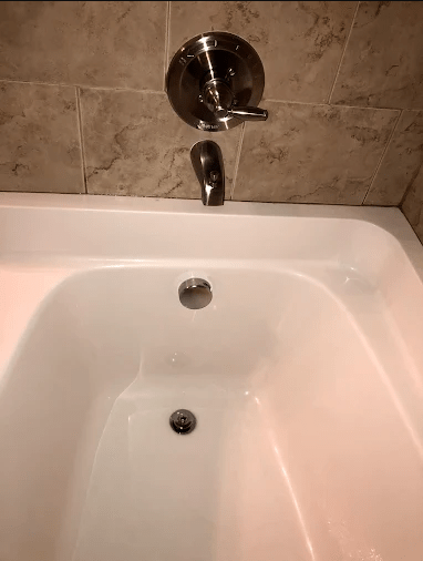 A modern bathtub with a chrome faucet and shower diverter, featuring beige tiled walls. The clean, minimal design emphasizes relaxation.