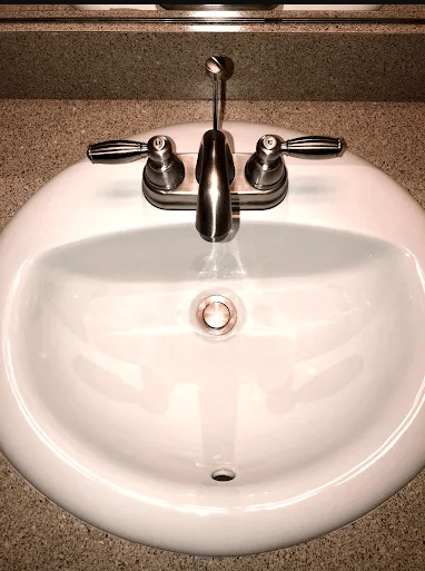 White sink with chrome faucet and handles, set on a textured countertop. Relevant for showing bathroom fixtures and design.