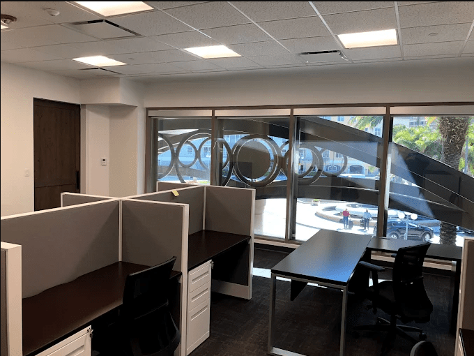 Modern office workspace featuring empty desks with dividers and large windows showing an outdoor view. Ideal for collaborative work environments.