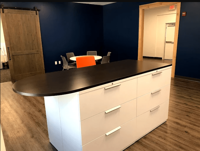 Modern reception area featuring a sleek white desk with a black countertop, surrounded by a cozy sitting area and a deep blue wall.
