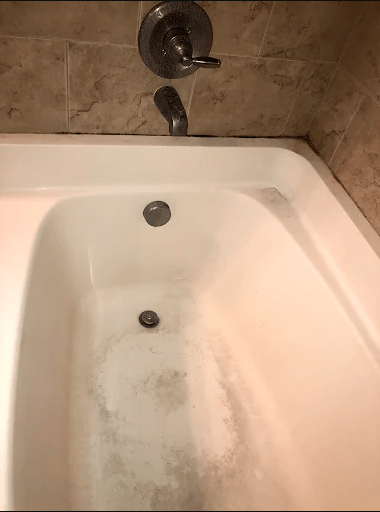 A clean, empty bathtub with a silver tap and drain in a tiled bathroom. The image highlights the bathtub's condition for maintenance or renovation context.