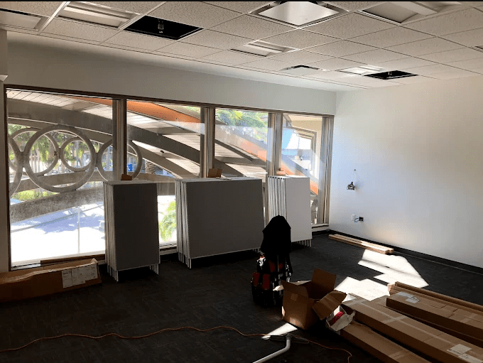 Empty office space with unassembled furniture and large windows showcasing an architectural feature. Natural light illuminates the area.