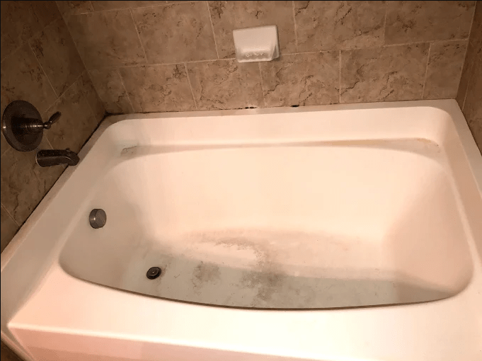 Bathtub with stained bottom and tiled walls, indicating wear. Relevant for a home maintenance or cleaning guide.
