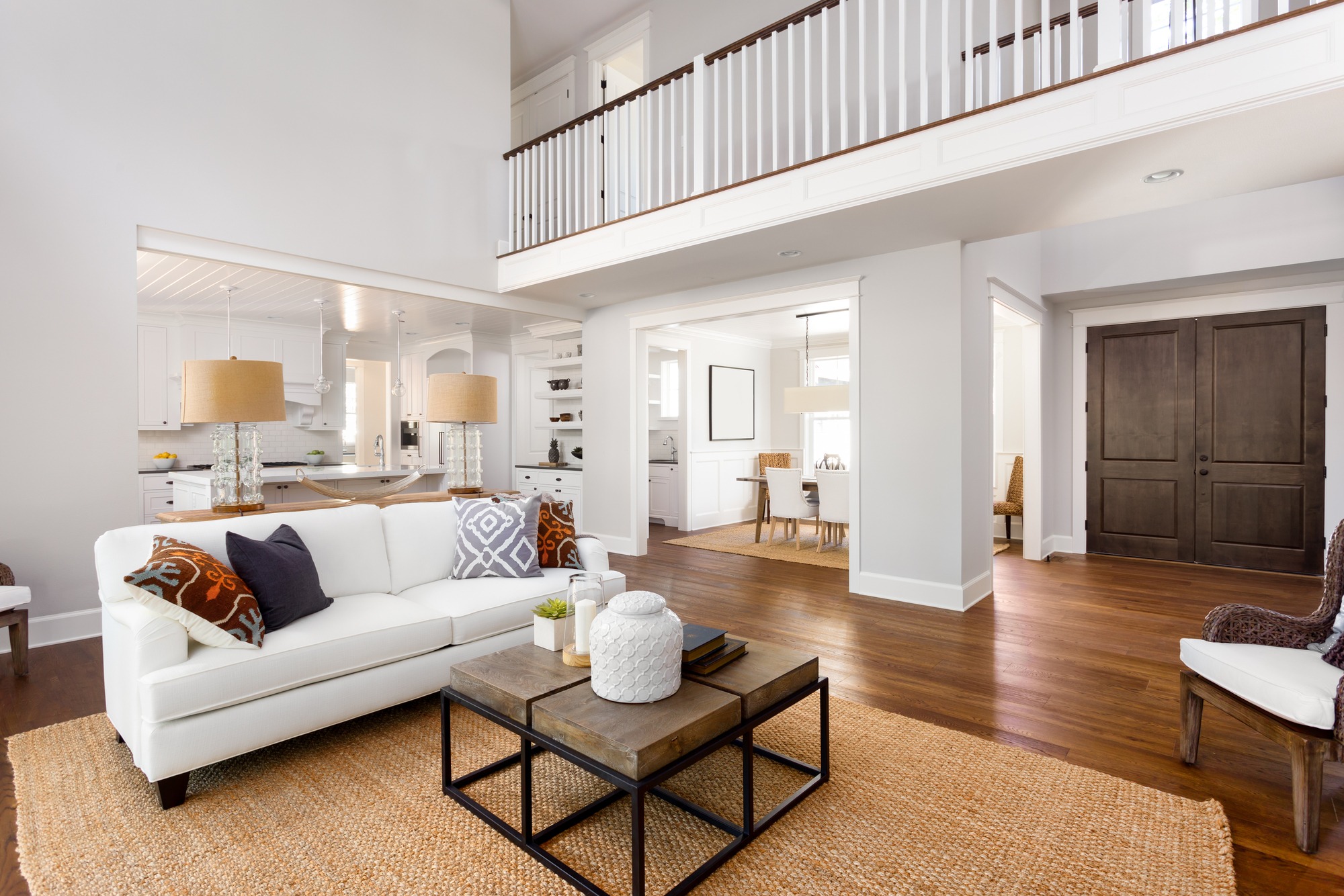 Bright, modern living room featuring a white sofa with decorative pillows, a rustic coffee table, and open access to a stylish kitchen and dining area.